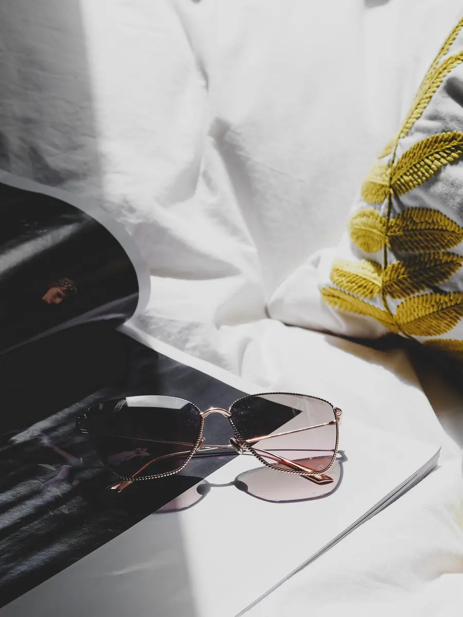 Sunglasses resting on white linen beside a magazine