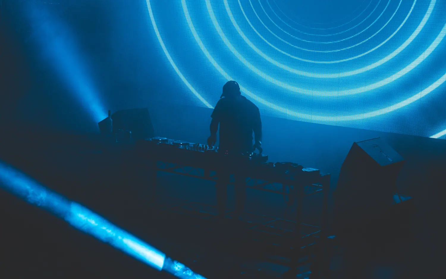 DJ silhouetted against glowing blue neon rings on a stage